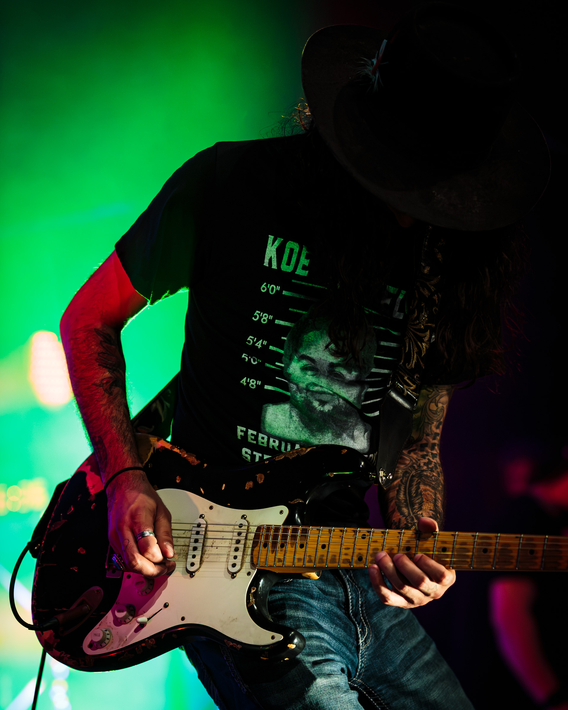 A guitarist playing a heavily worn electric guitar under stage lights